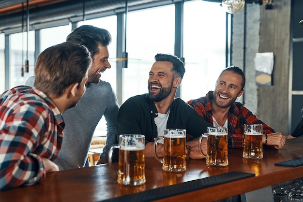 Premium Photo | Happy young men in casual clothing drinking beer and ...