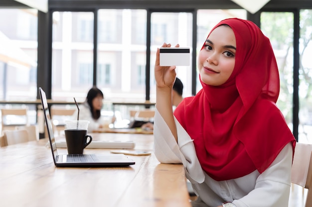 Download Happy young muslim woman red hijab hand showing credit card mockup in cafe. | Premium Photo