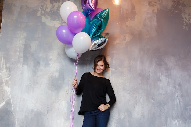 Happy young woman with colorful balloons near an empty gray concrete wall Free Photo