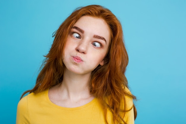 Headshot Portrait of happy ginger red hair girl with funny face looking at camera. Pastel blue background. Copy Space. Free Photo