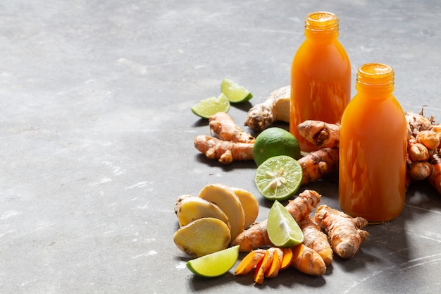 Healthy drink from turmeric and ginger roots and lime in small bottles on grey concrete wall. Premium Photo