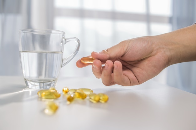 healthy lifestyle, medicine, nutritional supplements and people concept - close up of male hands holding pills with cod liver oil capsules and water glass Free Photo