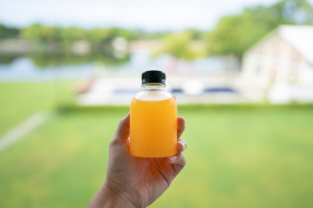 健康的なオレンジジュースのデトックス 手と緑の自然の背景に新鮮なオレンジ色のボトルのクローズアップ プレミアム写真