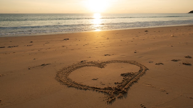 ビーチのハートのシンボル 夕日や日の出の空の美しい光の自然の風景の上のビーチの砂に手描きのハート プレミアム写真