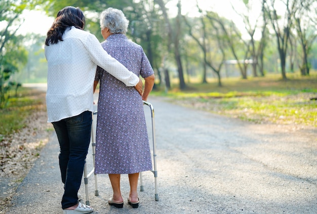 Help and care asian senior woman use walker while walking at park. Premium Photo