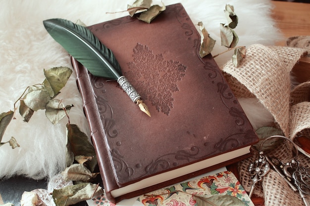 Colpo di alto angolo di una penna d'oca su un vecchio libro coperto di petali di fiori secchi Foto Gratuite