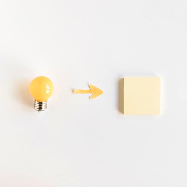 High angle view of arrow symbol between light bulb and adhesive note Free Photo