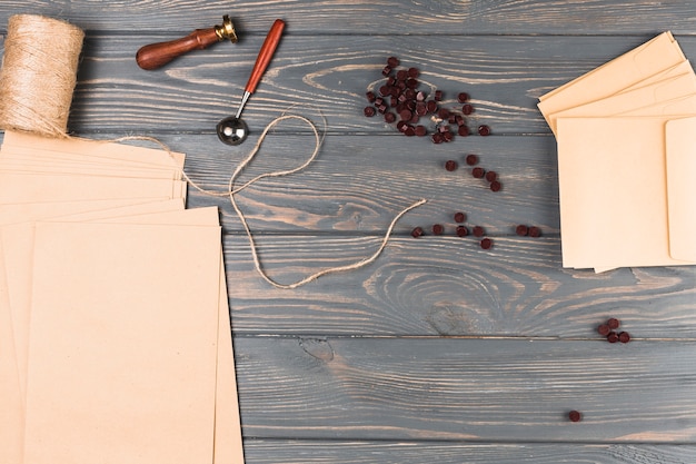 High angle view of brown wax; string spool; seal stamp; blank envelop card on wooden table Free Photo