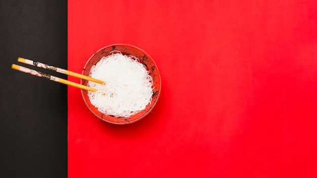 High angle view of white vermicelli in bowl with chopsticks over dual backdrop Free Photo