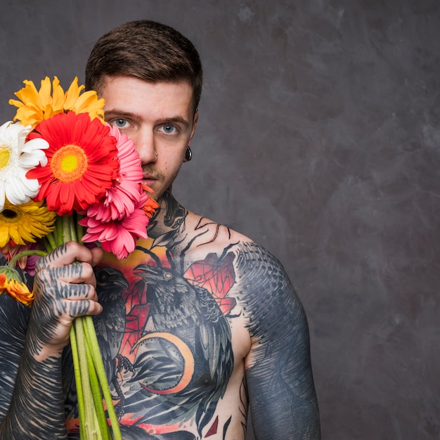 無料の写真 流行に敏感な刺青の若い男がカラフルなガーベラの花を保持