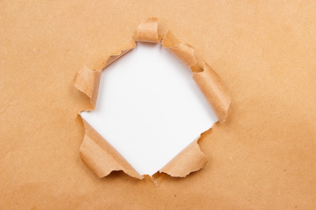 Hole into brown craft paper sheet with torn edges. Premium Photo