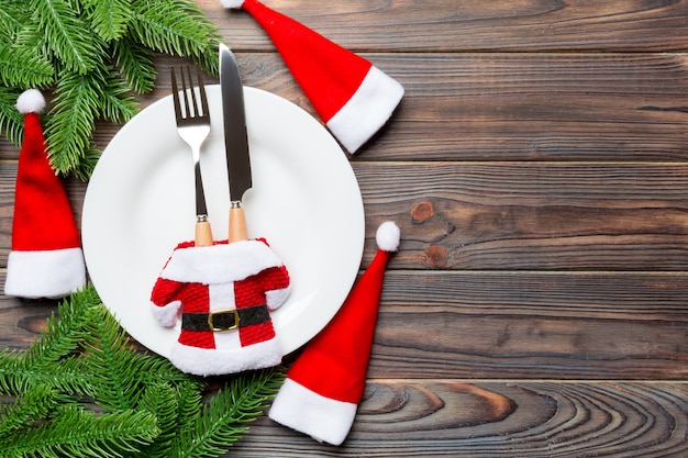 Premium Photo Holiday Composition Of Plate And Flatware Decorated With Santa Hat And Clothes On Wooden Background