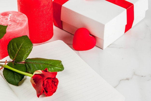 Holiday , valentine's day. bouquet of red roses, tie with a red ribbon, with blank notepad, wrapped gift box and red candle. on a white marble table, copyspace top view Premium Photo