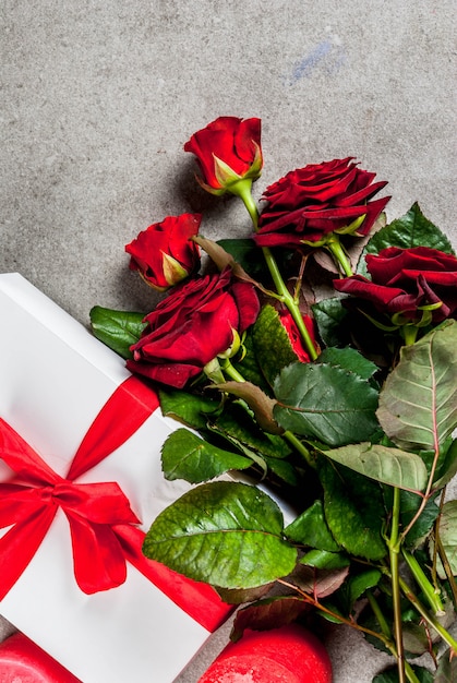 Holiday , valentine's day. bouquet of red roses, tie with a red ribbon, with wrapped gift box and red candle. on a gray stone table, copyspace top view Premium Photo