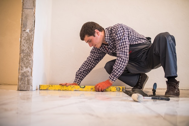 Home tile improvement - handyman with level laying down tile floor Free Photo