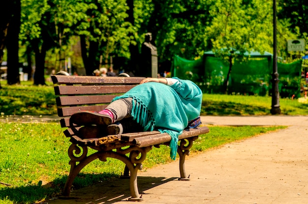 春の日に公立公園のベンチで寝そべって寝るホームレスの女性難民 プレミアム写真