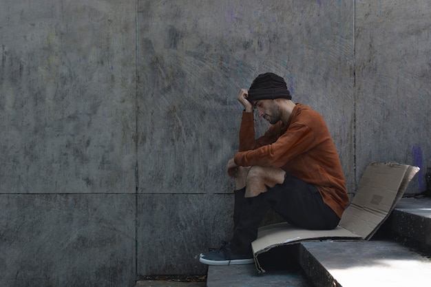 Homeless man sitting sideways on cardboard Free Photo