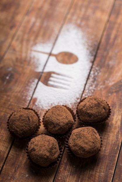 Homemade chocolate truffle candies with cocoa powder near the spoon and fork shape on sugar powder Free Photo