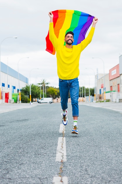 Homosexual running down road holding lgbt flag over head Free Photo