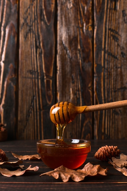 Honey flows from a stick into a jar. rustic sweet autumn photo, wooden background and dry leaves, copyspace. Premium Photo