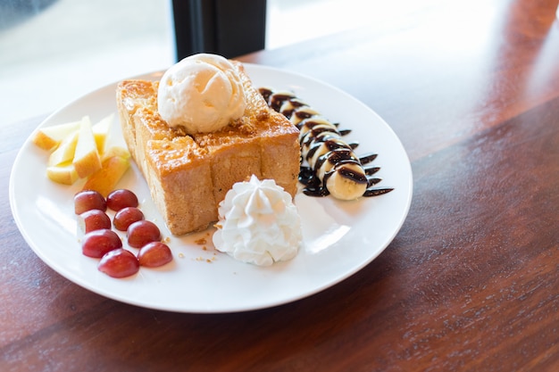 Honey toast with vanilla ice cream, whipped cream and chocolate syrup. served with banana, grape and apple Premium Photo