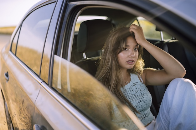 フィールドで車の前部座席でポーズをとる美しい若い白人女性の水平方向のショット 無料の写真