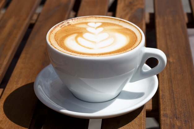 Hot cappuccino with froth and pattern on wooden background, side view Premium Photo