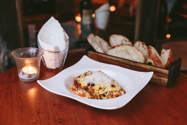 Hot served lasagne topping with mozzarella cheese served with sliced bread in wooden box. Premium Photo