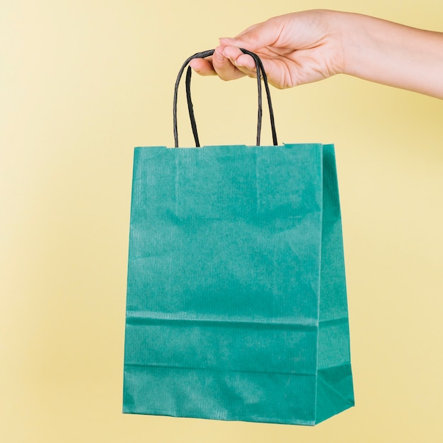 Download Premium Photo Human Hand Holding Green Paper Shopping Bag On Yellow Backdrop PSD Mockup Templates