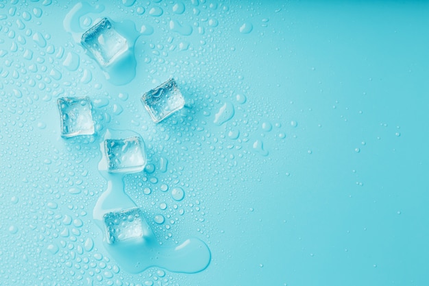 Ice cubes with water drops scattered on a blue background, top view. Premium Photo