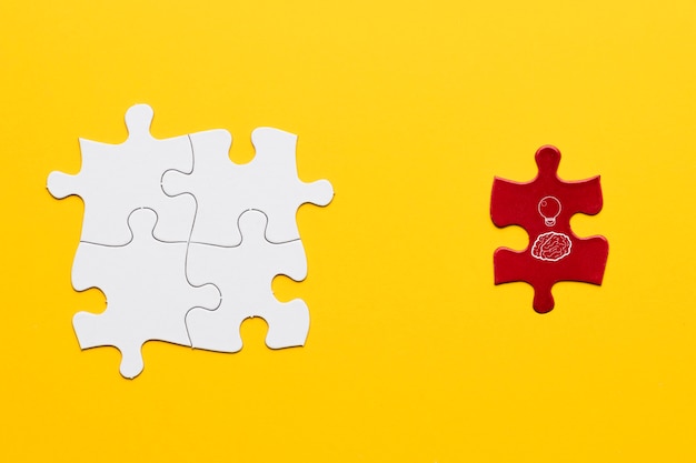 Idea icon on red puzzle piece standing near white joint puzzle piece over yellow backdrop Free Photo