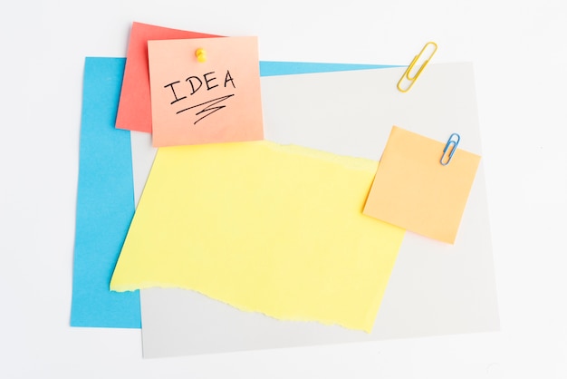 Idea text written on sticky note with pushpin and paperclip on white board Free Photo