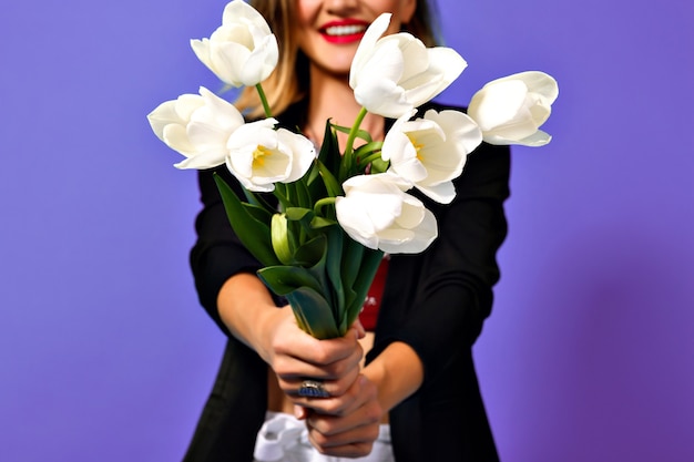 紫色の背景に分離された黒いジャケットの若いファッショナブルな女性の手に白いチューリップの花束の画像 無料の写真
