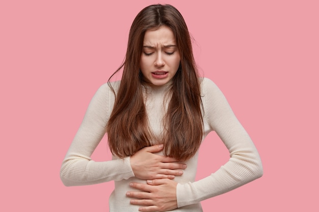 Image of unhappy woman suffers from stomachache after eating spoiled food, feels discomfort in belly, has disorder Free Photo