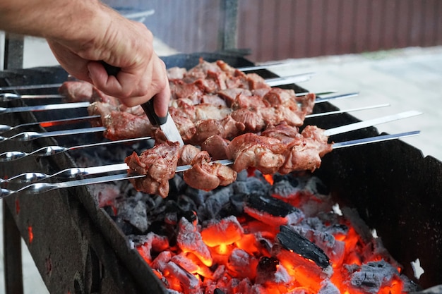 夏にバーベキューはグリルで調理されます 串刺しの肉 石炭からの煙 プレミアム写真