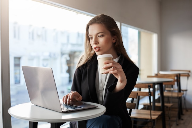 カフェに座って コーヒーを飲みながらラップトップに入力して魅力的なヨーロッパの女性の屋内ポートレート 無料の写真