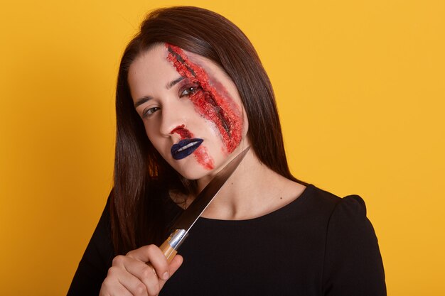 彼女の首の近くのナイフと彼女の顔に血の傷を持つブルネットの女性の屋内撮影 プレミアム写真