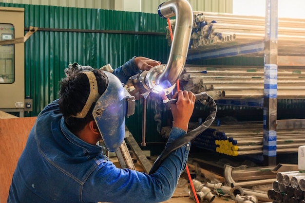 Industrial worker with protective mask welding metal piping using tig welder Premium Photo