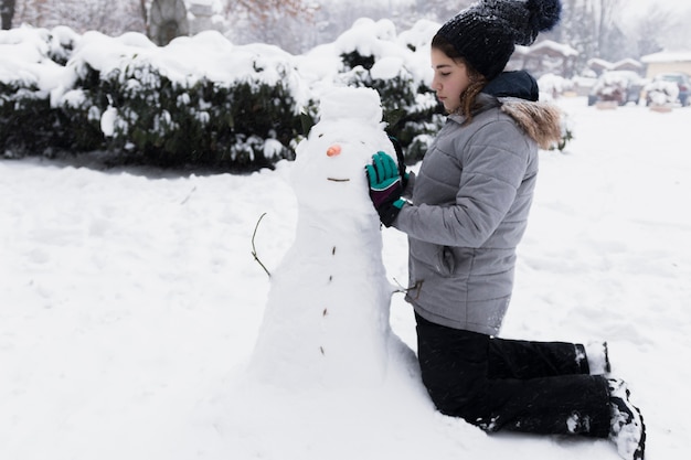 冬の雪だるまに触れる無邪気な女の子 無料の写真