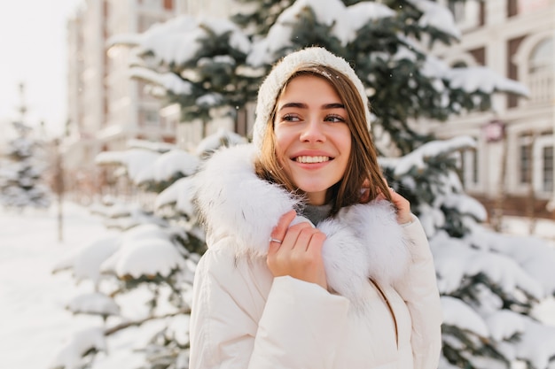 インスピレーションを得たヨーロッパの女性は 自然の景色を楽しみながら白い冬の服装を着ています 笑みを浮かべて見事な白人女性モデルの屋外のポートレート 無料の写真