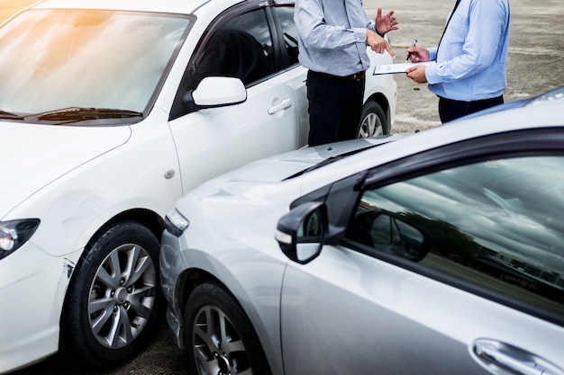 Insurance agent writing on clipboard while examining car after accident Premium Photo