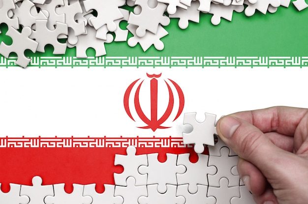 Iran flag  is depicted on a table on which the human hand folds a puzzle of white color Premium Phot