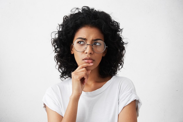 Isolated portrait of stylish young mixed race woman with dark shaggy hair touching her chin Free Photo