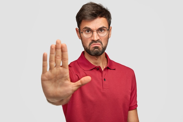 It`s forbidden! angry displeased young male frowns face, shows stop gesture, keeps palm in front, tries to prevent himeself from something bad and unpleasant, wears casual t-shirt, isolated on white Free Photo