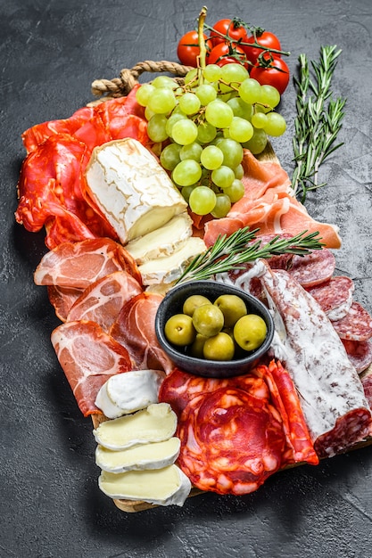 イタリアの前菜 生ハム ハム パルマ ヤギ カマンベールチーズ オリーブ ブドウの木製まな板 前菜 上面図 プレミアム写真