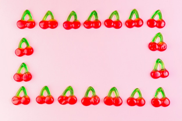 Jelly cherry candies forming rectangular shape frame on pink backdrop Free Photo