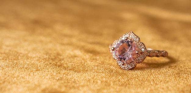 金色の生地の背景にジュエリーピンクダイヤモンドリングをクローズアップ プレミアム写真