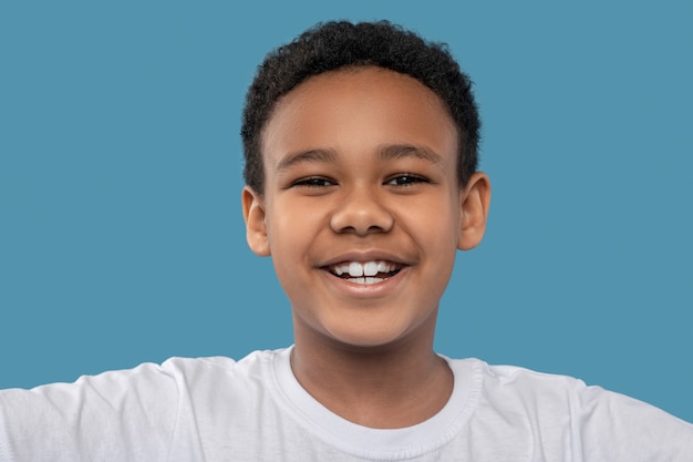 Premium Photo Joy Mood Joyful African American Boy With Black Curly Hair With Toothy Smile On Blue Background