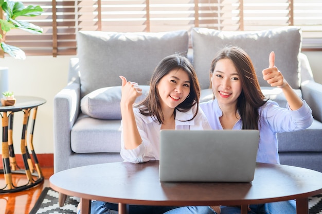 Joyful asian females using a laptop together Premium Photo