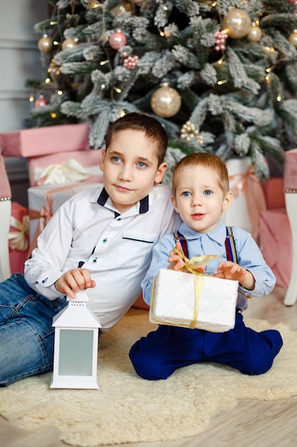 クリスマスプレゼントを開くうれしそうな子供たち 居心地の良い暖かい冬の夜 クリスマスイブの家族 ギフトボックスとクリスマス ツリーの下の子供たち 装飾されたリビングルーム 家にクリスマスギフトボックスを持つかわいい子供たち プレミアム写真